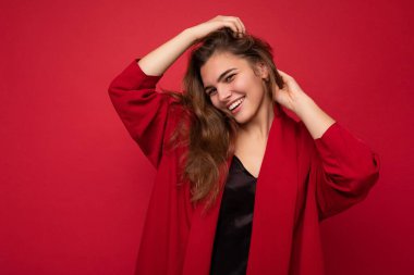 Güzel, mutlu, gülümseyen, kırmızı hırkalı, esmer bir kadının fotoğrafı. Kırmızı arka planda yalnız poz veren kaygısız seksi kadın. Pozitif model samimi duyguları gösterir