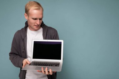 Bilgisayarlı yakışıklı sarışının yakın plan portresi. Mavi arkaplanda izole edilmiş netbook klavyesine bakıyor.