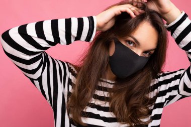 El yapımı pamuklu yüz maskesi takan çekici genç bir kadının fotoğrafı renkli arka plan duvarından izole edilmiş. COVID-19 'a karşı koruma