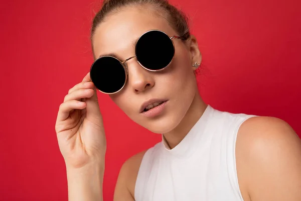 Photo shot of beautiful young blonde woman wearing casual clothes and stylish sunglasses isolated over colorful background looking at camera — Stock Photo, Image