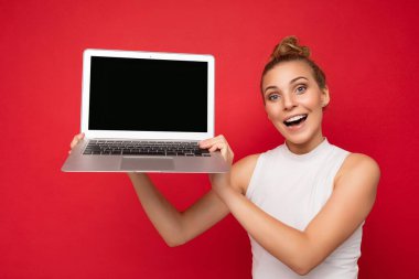 Mutlu, şaşkın, gülümseyen, saçları toplanmış, kameraya bakan, elinde boş ekran bilgisayarı olan güzel, sarışın bir kadın.