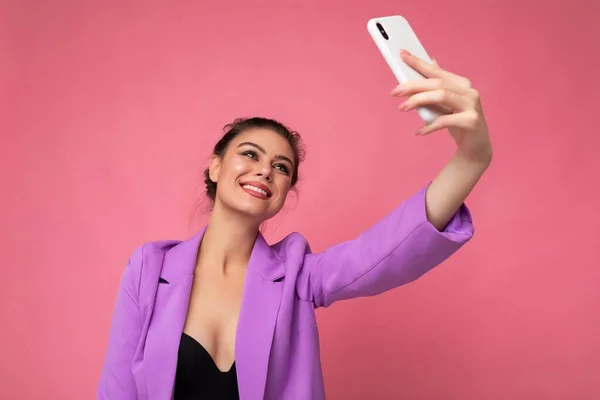 Attractive charming young happy woman holding and using mobile phone taking selfie wearing stylish clothes isolated over wall background — Stock Photo, Image