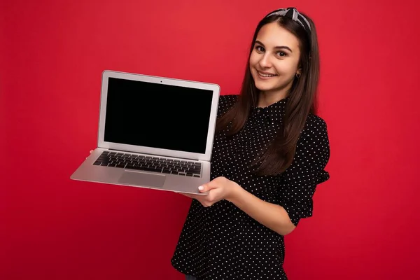 Fotografie de fată frumoasă zâmbitoare purtând haine negre ținând laptop-ul computerului uitându-se la camera izolată pe fundal de perete colorat — Fotografie, imagine de stoc