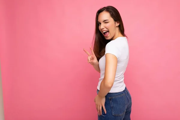 若い美しいブルネットの女性。カジュアルな夏の白いTシャツの流行の女性。肯定的な女性は顔の誠実な感情を示しています。ピンクの背景にフリースペースで隔離された面白いモデル — ストック写真