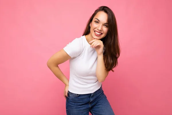 Foto portrét mladé krásné usmívající se hipster bruneta žena v bílém tričku s maketou. Sexy bezstarostná žena pózující izolované blízko růžové stěny s prázdným prostorem ve studiu. Kladný model — Stock fotografie