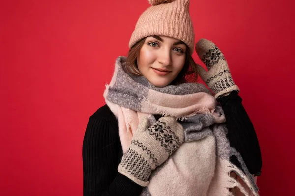 Shot of beautiful happy cute young brunette female person isolated over red background wall wearing winter scarf mittens and warm hat looking at camera — Stock fotografie