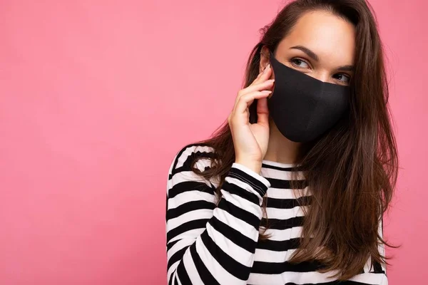 Молодая красивая женщина в многоразовой вирусной защитной маске на лице против коронавируса изолированы на розовом фоне стены — стоковое фото