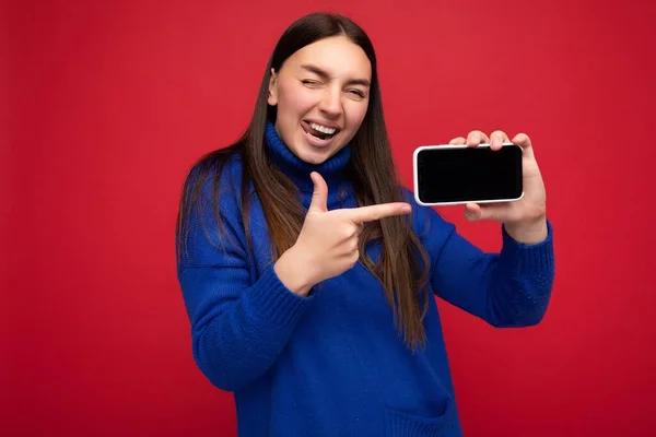 Foto de sexy bonita sorridente jovem boa aparência vestindo roupa elegante casual em pé isolado no fundo com espaço de cópia segurando smartphone mostrando telefone na mão com tela vazia — Fotografia de Stock