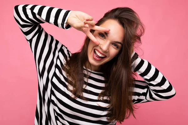 Fénykép fiatal európai pozitív mosolygós győztes boldog vicces gyönyörű barna nő őszinte érzelmek visel alkalmi csíkos pulóver elszigetelt rózsaszín háttér másolási hely — Stock Fotó