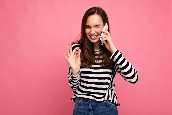 Kacsintás Elég boldog fiatal nő beszél a telefonon visel csíkos pulóver elszigetelt a háttérben fénymásolás hely mutatja rendben gesztus nézi kamera — Stock Fotó