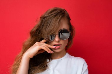 Güzel, genç, sarışın, sıradan kıyafetler giyen ve renkli arka planda izole edilmiş güneş gözlüğü takan güzel bir kadının yakın plan fotoğrafı.
