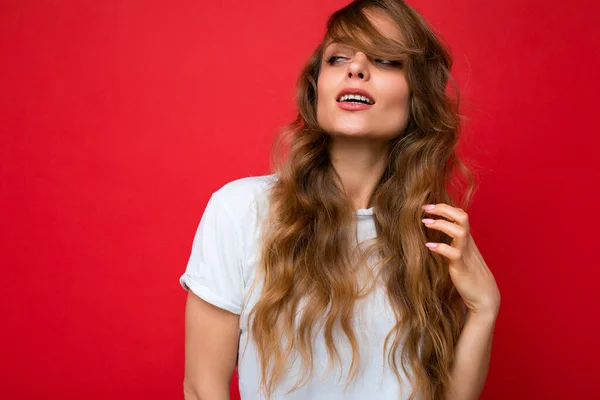 Jovem bela mulher loira encaracolado com expressão sexy, rosto alegre e feliz vestindo casual t-shirt branca isolada sobre fundo vermelho com espaço de cópia — Fotografia de Stock