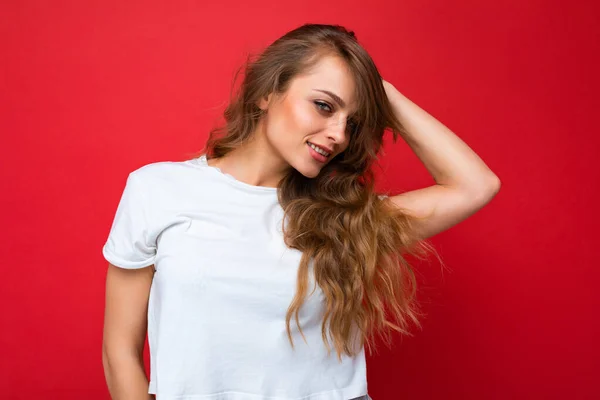 Ung vacker lockigt blond kvinna med sexigt uttryck, glad och glad ansikte bär casual vit t-shirt isolerad över röd bakgrund med kopia utrymme — Stockfoto