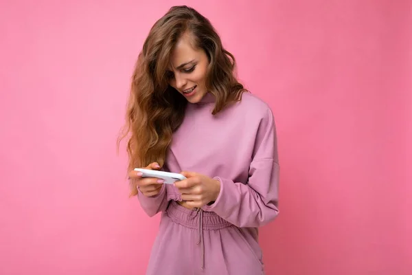 Foto tiro de atraente positiva boa aparência jovem mulher vestindo roupa elegante casual poising isolado no fundo com espaço vazio segurando na mão e usando sms mensagens de telefone móvel olhando para — Fotografia de Stock