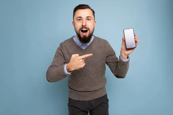 Foto de bonito sorridente adulto masculino pessoa bonita vestindo roupas casuais em pé isolado no fundo com espaço de cópia segurando smartphone mostrando telefone na mão com tela vazia para — Fotografia de Stock