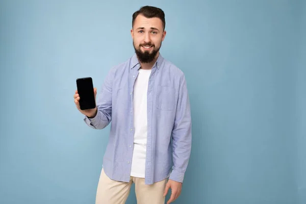 Bonito jovem legal feliz boa aparência vestindo roupas elegantes casuais de pé isolado sobre parede de fundo colorido segurando smartphone e mostrando telefone com tela vazia olhando — Fotografia de Stock