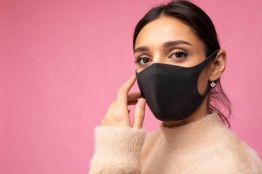 Yeniden kullanılabilir virüslü büyüleyici kadın yüzünde koronavirüs maskesi var. Pembe arka plan duvarında izole edilmiş.