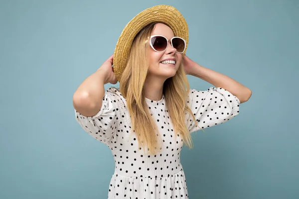 Zdjęcie atrakcyjnej szczęśliwej uśmiechniętej młodej blondynki noszącej letnie, luźne ubrania i stylowe okulary przeciwsłoneczne odizolowane od kolorowych ścian tła patrząc z boku — Zdjęcie stockowe