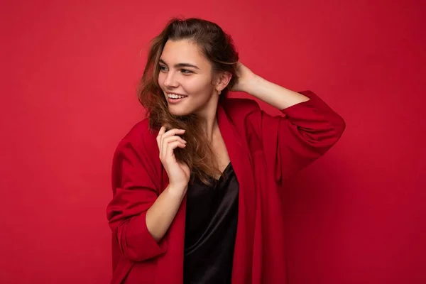Φωτογραφία πορτρέτο του όμορφη ευτυχισμένη αστεία νεαρή μελαχρινή γυναίκα σε κομψό κόκκινο ζακέτα. Σέξι ανέμελη γυναίκα που ποζάρει απομονωμένη σε κόκκινο φόντο. Θετικό μοντέλο δείχνει ειλικρινή συναισθήματα — Φωτογραφία Αρχείου