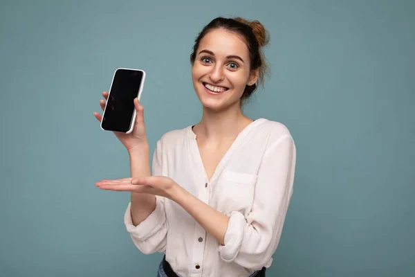 아름다운 미소를 가진 젊은 여성 이 평범 한 스타일의 복장을 한 채빈 화면을 보여 주는 스마트폰을 손에 들고 복사본 공간에 고립된 채서 있는 아름다운 사진 — 스톡 사진