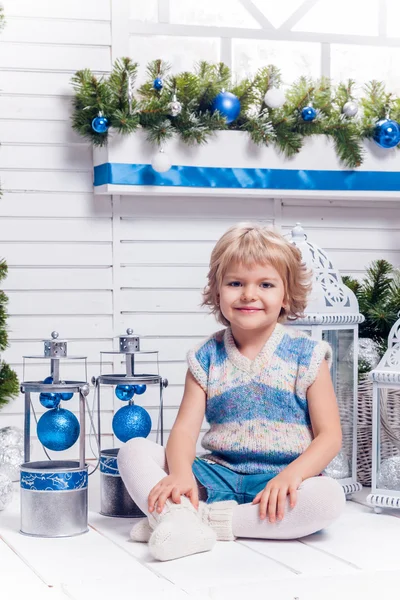 Pequeña chica bonita sonriente sentada junto a un árbol de Navidad y — Foto de Stock