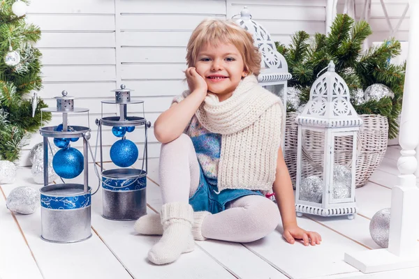 Piccola bella ragazza sorridente seduta accanto a un albero di Natale e — Foto Stock