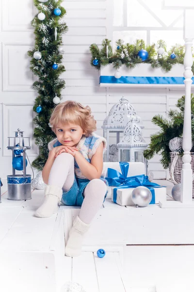 Pequeña chica bonita sonriente sentada junto a un árbol de Navidad y —  Fotos de Stock