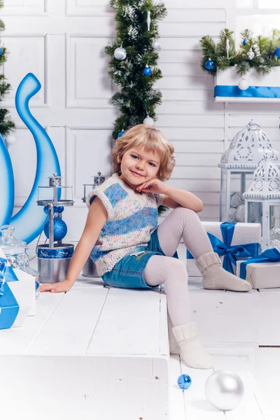 Pequena menina bonita sorridente sentada ao lado de uma árvore de Natal e — Fotografia de Stock