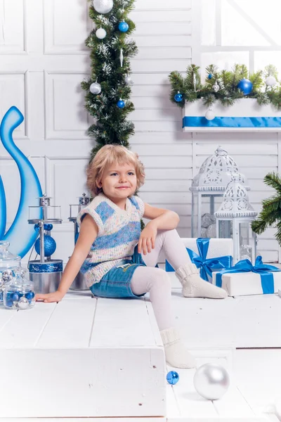 Lilla leende vackra flicka sitter bredvid en julgran och — Stockfoto