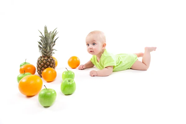 Ładny uśmiechający się dziecka leżącego na brzuchu, wśród owoców i patrząc — Zdjęcie stockowe