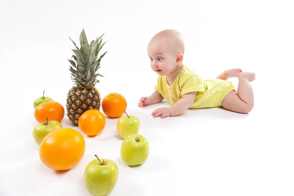 Милый улыбающийся здоровый ребенок лежит на белом фоне среди фруктов — стоковое фото