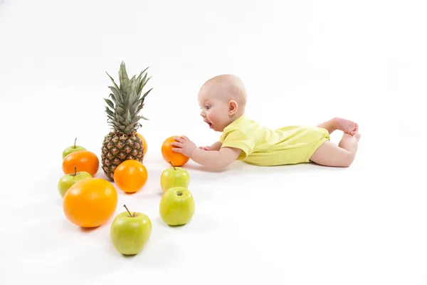 Cute smiling healthy child lies on a white background among frui — Stock Photo, Image