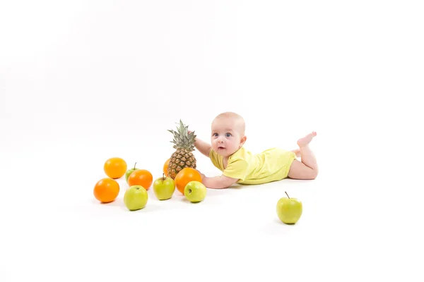 Милый улыбающийся здоровый ребенок лежит на белом фоне среди фруктов — стоковое фото
