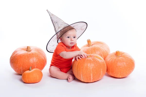 Baby in orange t-shirt on a white background sits next to pumpki — Zdjęcie stockowe
