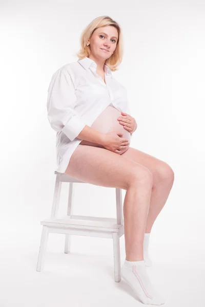 Embarazada rubia en camisa blanca y calcetines blancos sentado en un taburete —  Fotos de Stock