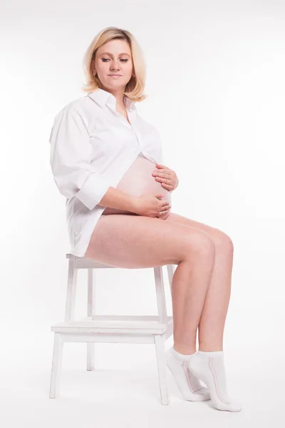 Pregnant blonde in white shirt and white socks sitting on a stoo — Zdjęcie stockowe