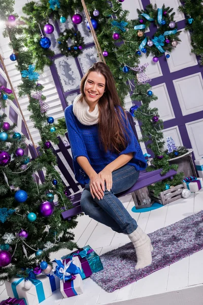 Charming brunette in jeans and a blue sweater sits on a swing on — Zdjęcie stockowe