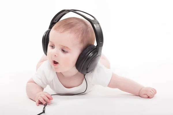 Encantador bebé sobre un fondo blanco con auriculares escuchando — Foto de Stock