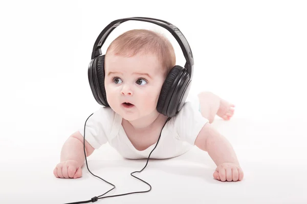 Encantador bebé sobre un fondo blanco con auriculares escuchando — Foto de Stock