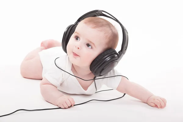 Encantador bebé sobre un fondo blanco con auriculares escuchando — Foto de Stock