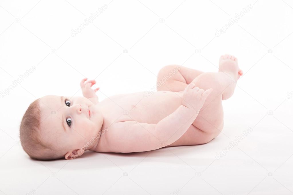 Naked baby lies on his back and looks at the camera.