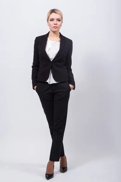 Ξανθιά κυρία επιχειρήσεων σε μαύρο κομψό κοστούμι στέκεται πάνω σε ένα λευκό β — Φωτογραφία Αρχείου