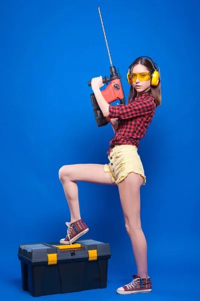 Девушка на синем фоне с молотком сверла и коробка с инструментами — стоковое фото