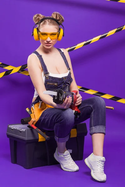 電気ジグソーと紫色の背景にセクシーなブロンドの女性 — ストック写真
