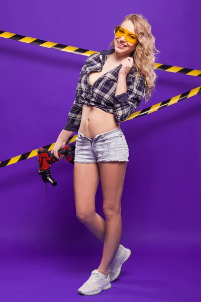 Sexy blonde construction worker with screwdriver on a purple bac — Stock Photo, Image