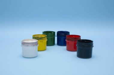 Mavi arka planda çok renkli boyalar olan plastik kavanozlar.. 