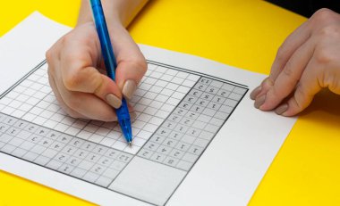 Bir kadın Japon bulmacasını çözüyor. Sarı arka planda Japon bulmacası. Yüksek kalite fotoğraf