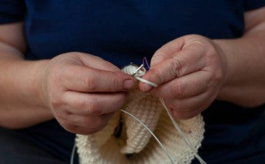 Kadın elleri örgü iğnesi ve iplik tutuyor. Örgü örüyorum. Bir kadın süveter, atkı ya da şapka örer. Ev yapımı ürün..