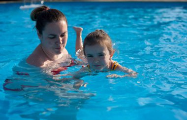 Anne küçük kızına yüzmeyi öğretiyor. Anne ve kızı havuzda yüzüyor. Sıcak ülkelerde dinlenin. Otelde dinlenin.