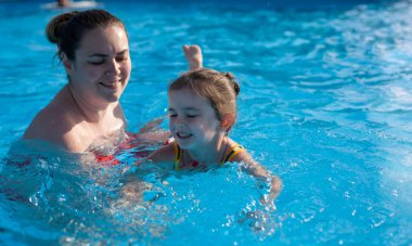 Anne küçük kızına yüzmeyi öğretiyor. Anne ve kızı havuzda yüzüyor. Sıcak ülkelerde dinlenin. Otelde dinlenin.